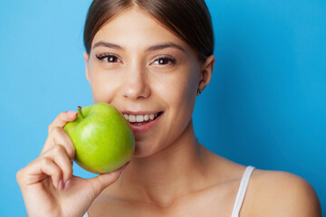 Portrait of a cheerful young woman with perfect smile eating green apple