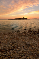 Fototapeta na wymiar Reddish sunset on round stone beach on the beach called Santo do Mar, in Galicia.
