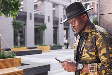 fashionable african man hold mobile phone in hands outdoors, chatting with someone or surfing the Net