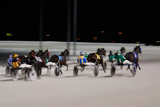 Cluster of harness racers speeding down the racecourse curve