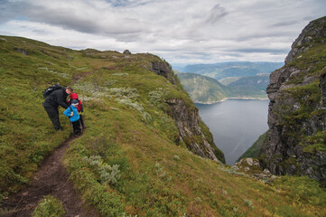 Fototapeta na wymiar Horizontal photo of the family of three is on their way to hike in the norwegian montains in the fjord
