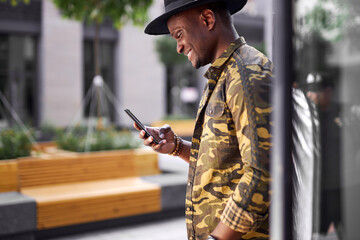 handsome dark-skinned man chatting with friend outdoors, young male look at smartphone and smile