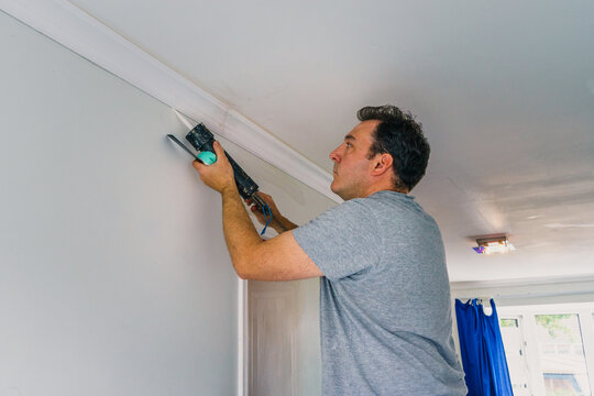young dark haired man filling cornice on ceiling with sealant gun