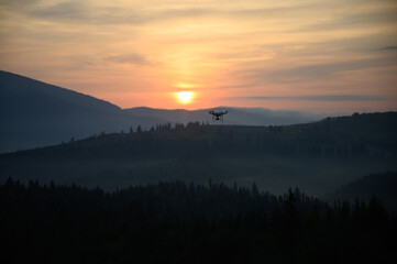 Silhouette Drone flying on mountain sunrise sky with cloud, Aerial photography. mountains landscape with sun and alpine pines. Sunrise
