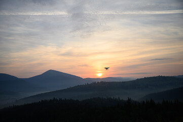 Silhouette Drone flying on mountain sunrise sky with cloud, Aerial photography. mountains landscape with sun and alpine pines. Sunrise
