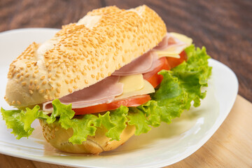 Sandwich of mayonnaise, cheese, ham, tomato and lettuce placed on a white plate on a rustic wooden table, selective focus.
