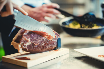 Detail shot of chef cook cutting Parma ham for use in a dish