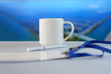 White cup, badge and pen on white table, soft blue background, business style