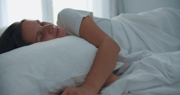 Happy woman waking up after sleep, lying in bed in the morning. Light bedroom. Close-up portrait of a woman. High quality 4k footage