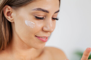 Obraz na płótnie Canvas Laughing girl applying moisturizing cream on her face.