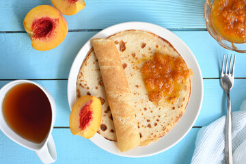 large pancakes with jam, tea and peaches on blue