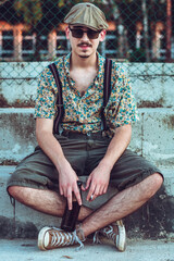 Young hipster man in retro clothing sits on the stairs with beer in his hands