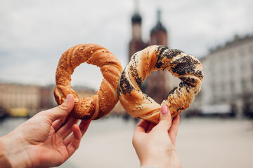 Couple of tourists holding bagels obwarzanek traditional polish cuisine snack on Market square in Krakow. Travel Europe