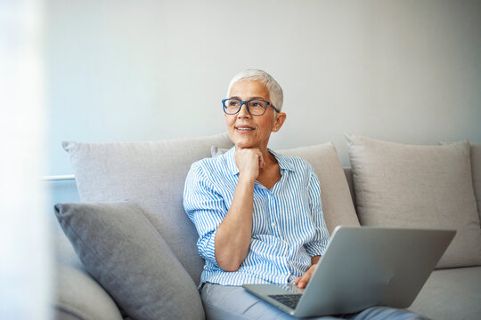 Portrait of a mature woman working on her laptop at home. Enjoying a little free time. Mature woman using laptop in the living room. Woman sitting on her couch using laptop