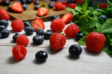 strawberries, raspberries and blueberries on a white wooden table with mint sprigs. bog whortleberry