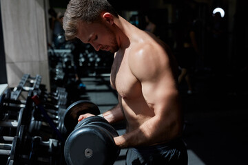 young muscular man in sportswear lift weights while working out in gym, strong guy exercises alone, side view