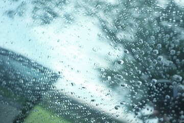 Blurred many rain drops on car window with heavy rainy day with dramatic weather and blurred green nature background 