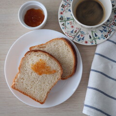 Morning toasts with apricot jam on white plates and served with a cup of black coffee. Wooden background and top view.