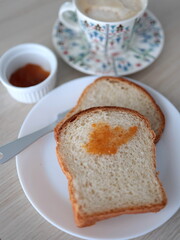 Homemade bread and apricot jam served with a cup of coffee latte with foam. A tasty and minimal refreshment in the afternoon.
