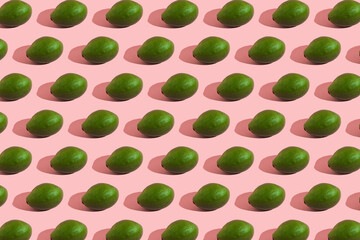 Trending style pattern of a whole green avocado on a pink background with hard light. Creative food texture.