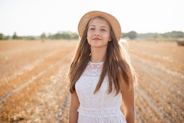Young girl in white dress and straw hat standing in an agricultural field after the harvest