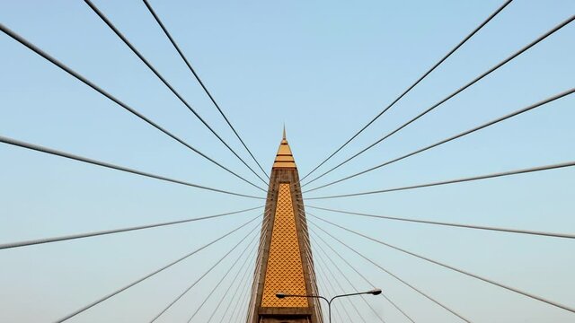 A ride under the supporting tower of the cable bridge. Concrete bridge pylon with parallel lines of steel cable. Construction Cable-stayed bridge against blue sky.