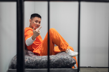 A crazy member of a Chinese mafia gang sits in a cell and shows an obscene gesture to the camera - obrazy, fototapety, plakaty