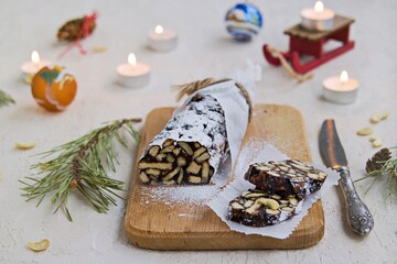 Dessert, chocolate salami with cookies and cashews in the New Year and Christmas style on a wooden board on a light concrete background.