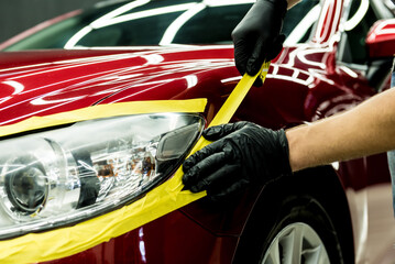 Car service worker applying protective tape on the car details before polishing.
