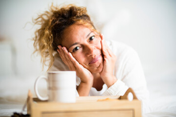 Cheerful beautiful young adult caucasian woman portrait lay down in the bedroom on the bed with cup...