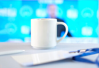 White cup, badge and pen on white table, soft blue background with shape of person , business concept