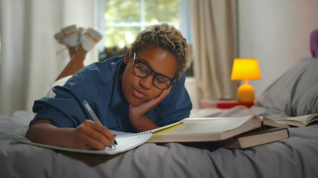 Pretty young african female student lying on bed studying at home