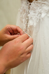 Female hands helping to fasten the bride's wedding dress on her back.