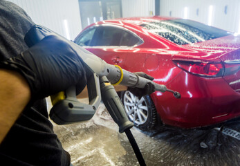 Worker washing car with high pressure water at a car wash.