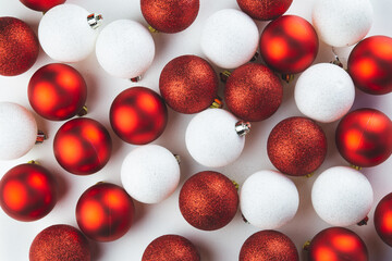 Red and white balls of Christmas tree decorations are scattered on a white table. New Year background, postcard. Flatly.