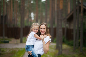 Happy smiling mother and her cute emotional little daughter child in white shirts and denim jeans are hugging and having fun outdoor in nature at countryside. Spending summer time with family.