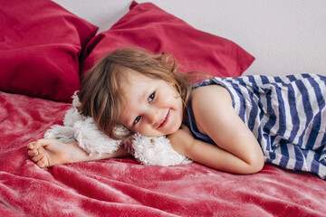 little three-year-old girl toddler lies in the bedroom on a pink bed and laughs