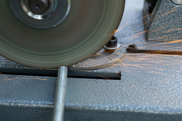The angle grinder cuts the metal pin. The angle grinder is mounted on a stand. Sparks fly from under the disk.