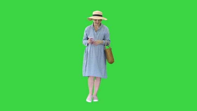 Young pregnant woman in trendy hat walking and using her phone on a Green Screen, Chroma Key.