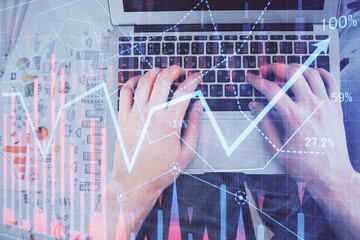 Double exposure of man's hands typing over laptop keyboard and forex chart hologram drawing. Top view. Financial markets concept.