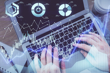 Double exposure of man's hands typing over computer keyboard and forex graph hologram drawing. Top...