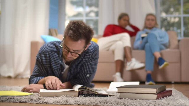 Portrait of concentrated male student reading textbook lying in carpet
