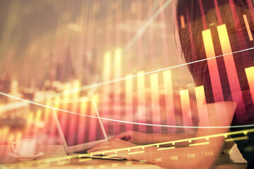 Double exposure of businesswoman hands typing on computer and forex chart hologram drawing....