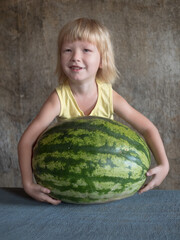 Fototapeta premium Funny blond boy hugs big watermelon lying on table with his hands