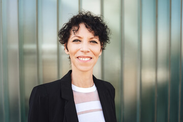 Fototapeta premium Close up portrait of smiling mature business woman in suit standing against green wall