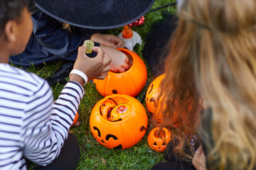 High angle view at group of kids wearing costumes taking candy from Halloween buckets outdoors,...