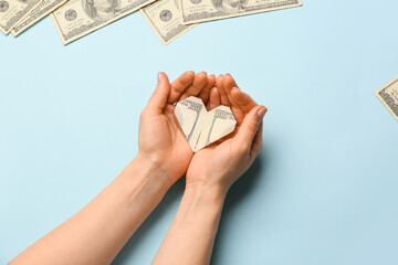 Female hands with origami heart made of dollar banknote on color background