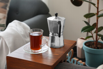 Cup of drink and coffee pot on armrest table in room