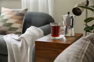 Cup of drink and coffee pot on armrest table in room