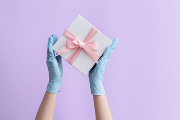 Hands in protective gloves and with gift box on color background